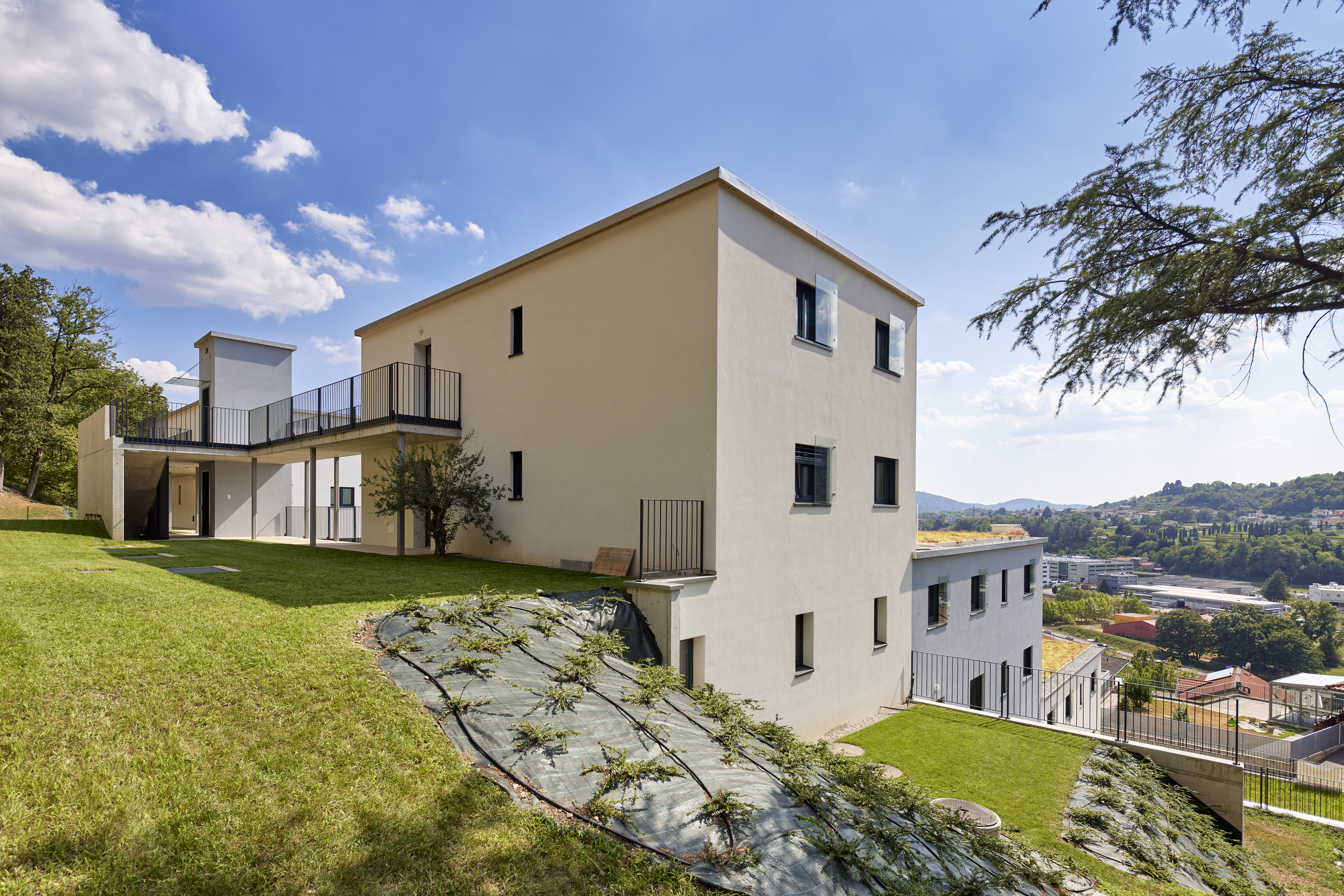 Modernes mehrstöckiges Wohnhaus an Hanglage mit gepflegter Grünfläche und Aussicht auf die Umgebung.