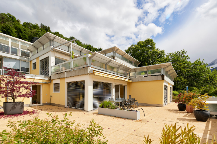 Modernes Wohnhaus mit grosszügigen Terrassen und Balkonen auf einem gepflegten Grundstück am Hang.