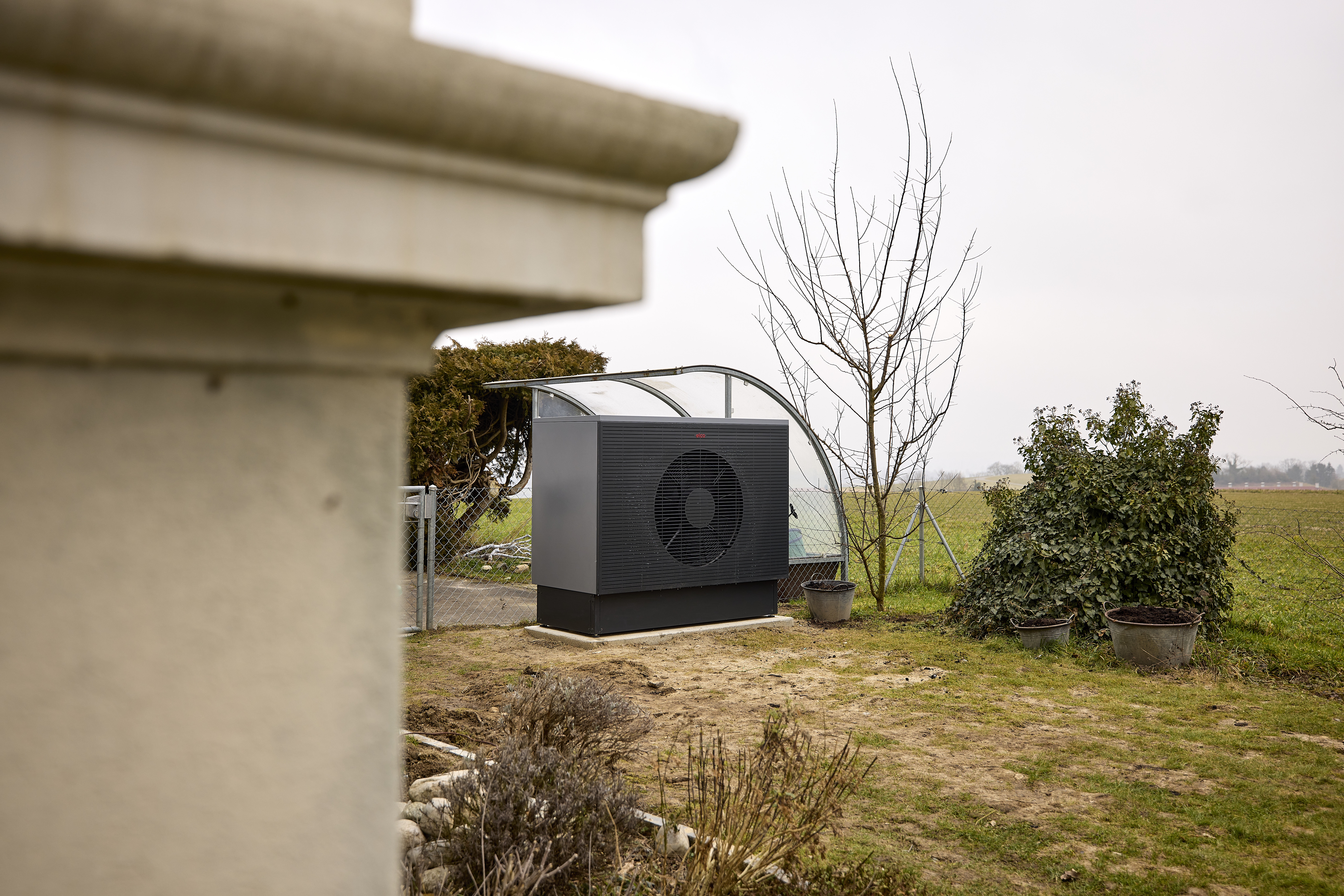 Ausseneinheit einer Wärmepumpe in einem Gartenbereich neben einer Wiese und Sträuchern.