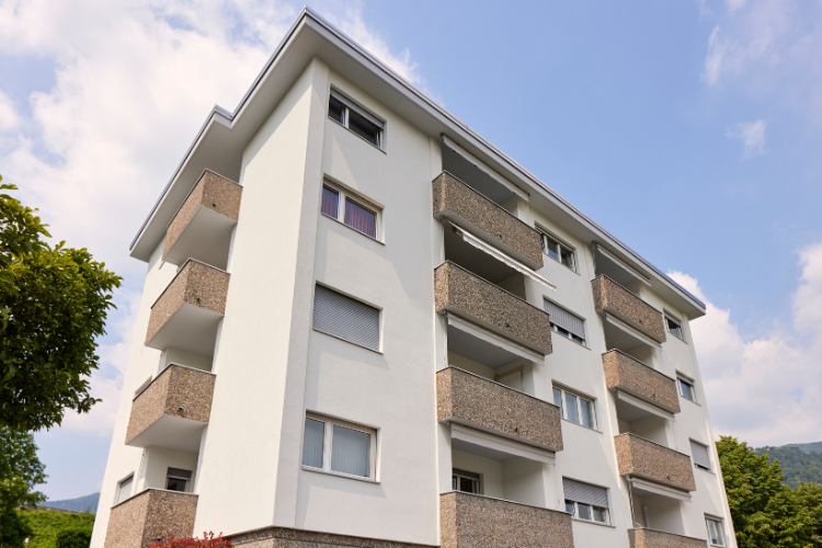 Mehrstöckiges Wohnhaus mit Balkonen und heller Fassade unter blauem Himmel.