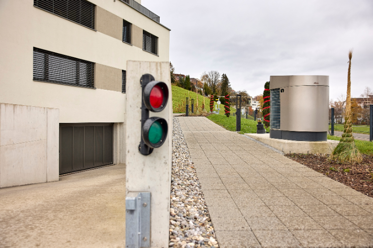 Feu de signalisation devant un immeuble résidentiel moderne avec chemin pavé et espaces verts.