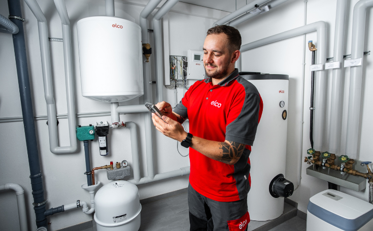 ELCO Servicetechniker mit REMOCON NET Fernbedienung vor Wärmepumpe
