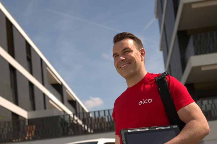 ELCO Servicetechniker in roter Arbeitskleidung vor einem modernen Gebäude.