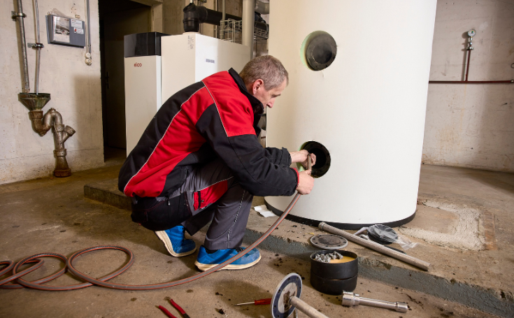 Fachperson arbeitet an einem grossen Warmwasserspeicher im Technikraum einer Heizungsanlage