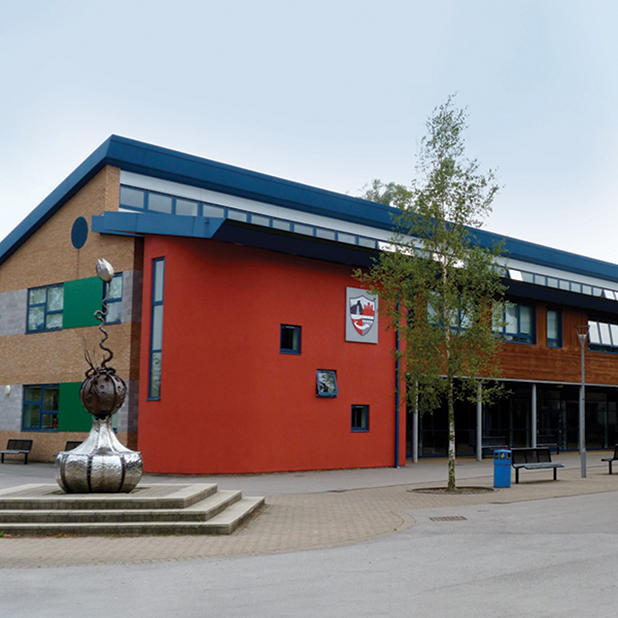 Aussenansicht des Gebäudes der Ripley Academy mit roter und brauner Fassade, Fenstern und einer Skulptur